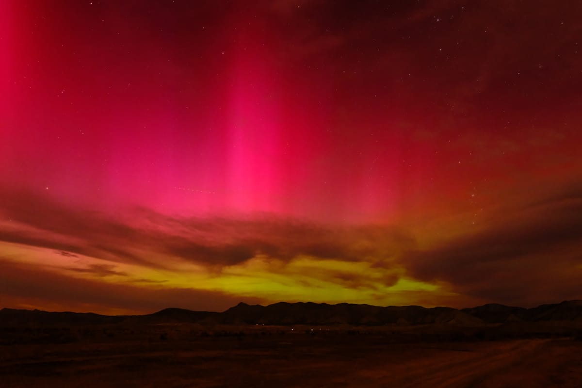 Pink, orange, red Aurora Borealis with the light of some stars shining through with mountains in the background