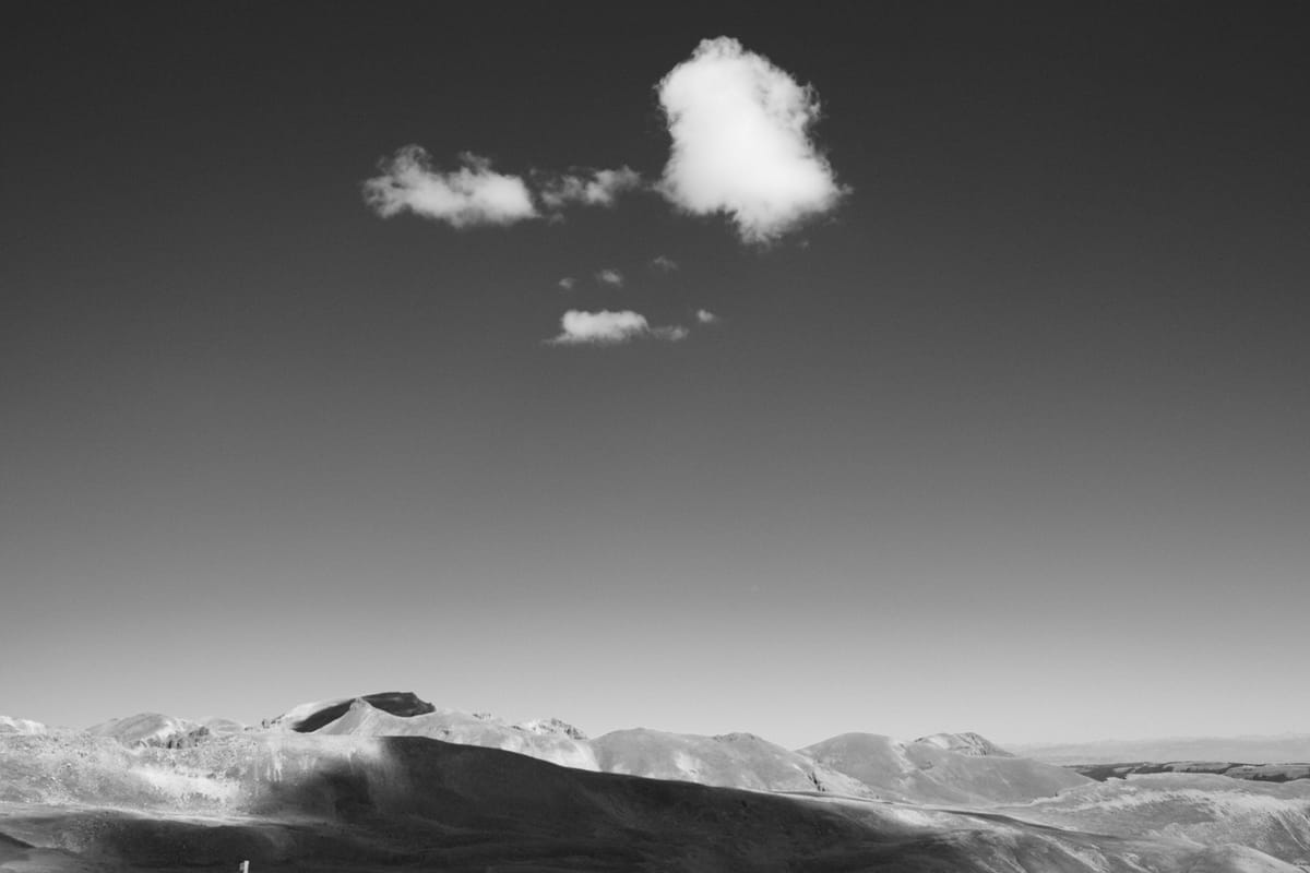 black and white above treeline view of a puffy cloud above mountains outside of Aspen, CO. 